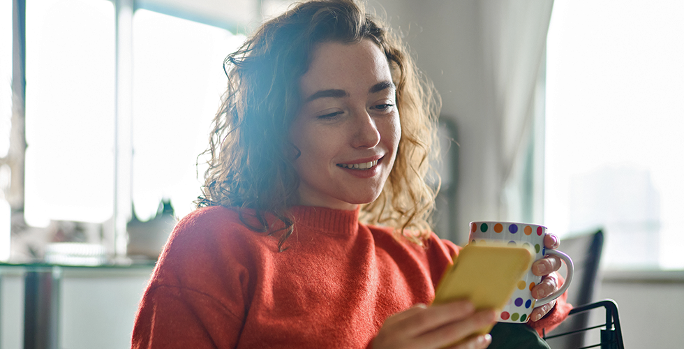 frau-mit-handy-und-tasse-auf-sofa